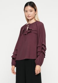 Mauve blouse met ruches bij de hals en mouwen, van een zachte stof en met een ontspannen pasvorm. Heeft een striksluiting bij de hals.