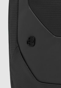 Zaino nero con tessuto strutturato e logo liscio e semilucido. La forma è angolare, con cuciture rinforzate e chiusura con zip.