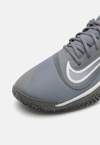 Graue SportSchuhe mit einer strukturierten Oberseite, ausgestattet mit einem weißen Swoosh-Logo, einer Gummisohle mit Profil für besseren Halt und grauen Schnürsenkeln, die farblich passend sind.