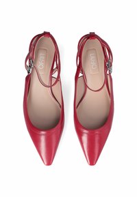 Décolleté slingback in pelle rossa con punta affusolata, caratterizzate da cinturini incrociati e un accento in fibbia silver. Texture liscia e design minimalista.