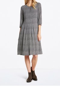 Vestido estampado en blanco y negro con mangas tres cuartos, falda con pliegues, escote redondo, combinado con botas tobilleras marrón oscuro.