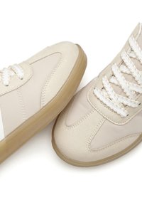 Beige sneakers featuring a mix of smooth and suede textures, round toe, white laces, and a flexible rubber sole.