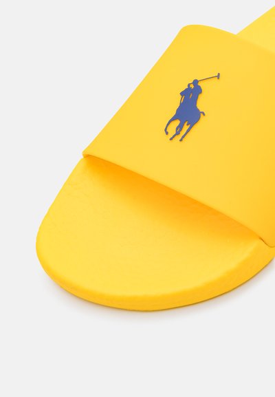 Chinelo amarelo feito de borracha suave, apresentando uma tira larga com um logotipo em relevo de um jogador de polo azul. Palmilha texturizada para melhor aderência.