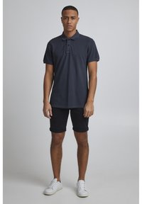 Námořnické polo tričko s límečkem a tříknoflíkovou légou, spárované s černými krátkými kalhotami s ohrnutými nohavicemi a bílými teniskami.