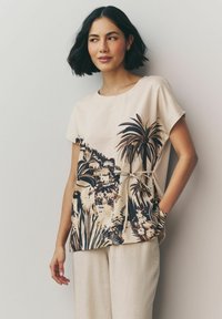 Beige kortærmet top med tropisk print i mørkebrun og creme, med en knyttet talje og sidelommer, lavet af letvægtsstof.