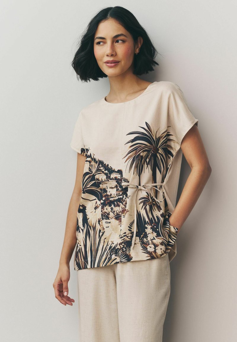 Beige kortærmet top med tropisk print i mørkebrun og creme, med en knyttet talje og sidelommer, lavet af letvægtsstof.