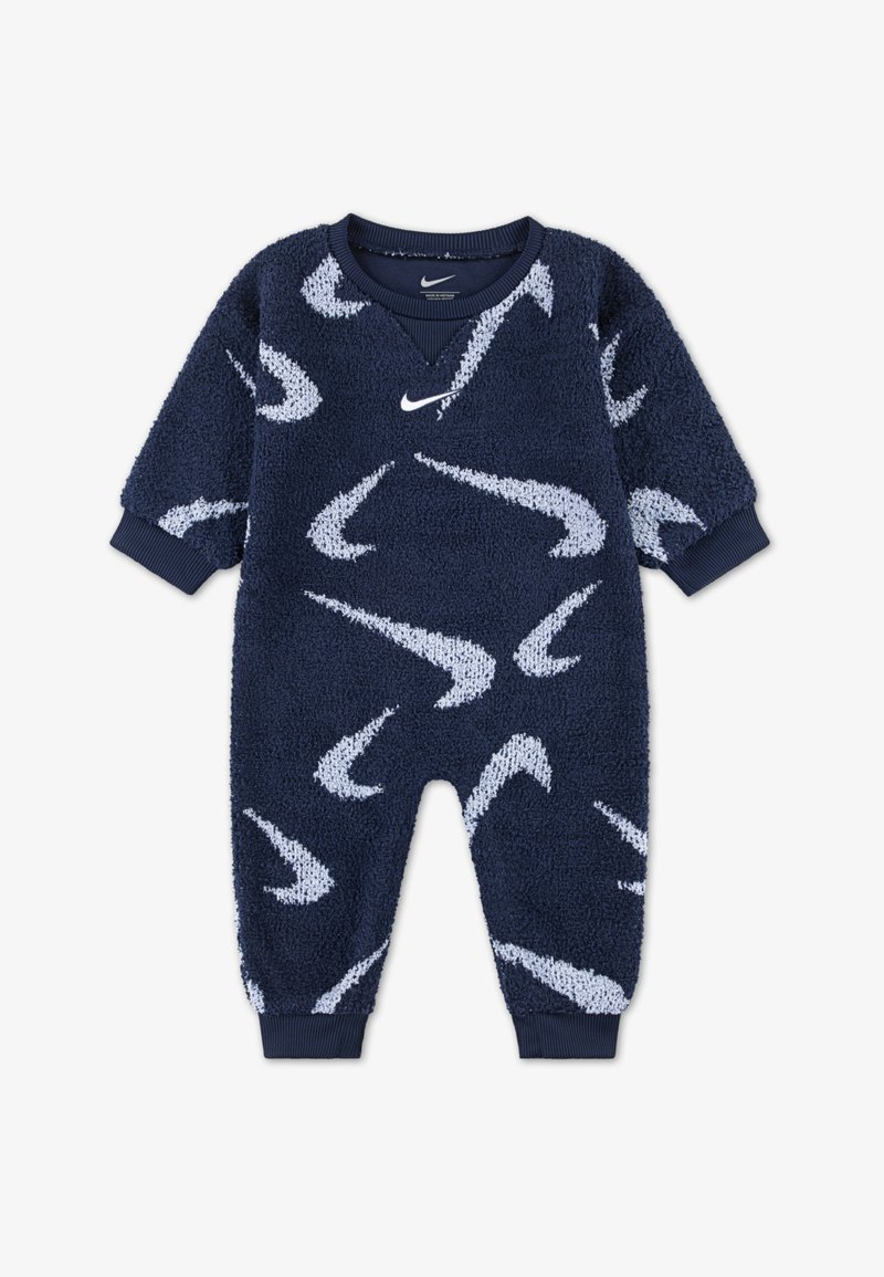 Tamsiai mėlynas flisinis kūdikio kostiumas su baltomis Nike swoosh rašmenimis, įsiūtomis rankogalių detalėmis ir V formos iškirpte. Minkšta tekstūra ir laisvas kirpimas suteikia patogumo.