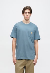 Modrá bavlněná trička s kulatým výstřihem, krátkými rukávy a náprsní kapsou s označením značky. Hladká textura s volným střihem.