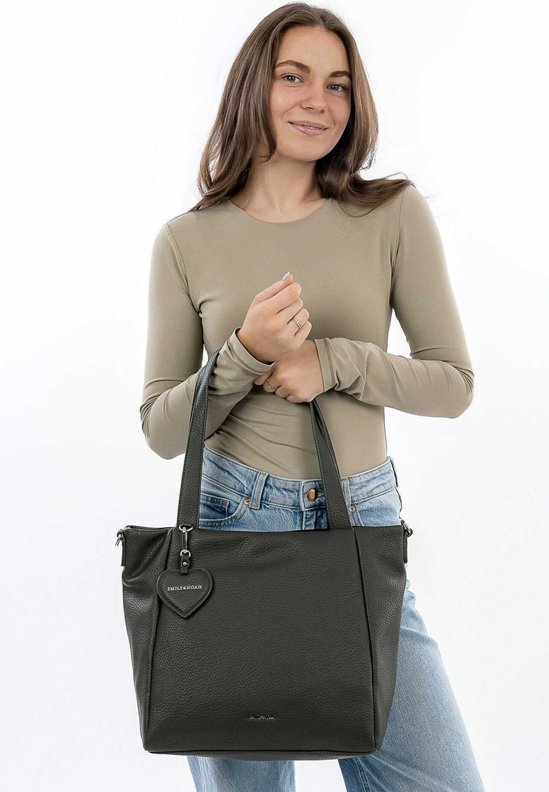 Borsa tote in pelle grigia scura con superficie testurizzata, due manici, chiusura con zip e un ciondolo a forma di cuore attaccato.