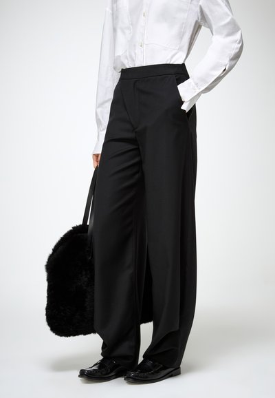 Juodos plačios kelnės su aukštu juosmeniu, pagamintos iš glotnios medžiagos. Derinamos su balta palaidine ir juodais batais, laikantis juodą kailinę rankinę.