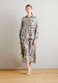 Dolga majica s ovratnikom v lahkem materialu z zapletenim paisley vzorcem v temno modrih in mehkih bež tonih. Kombinirano s sandali z naramnicami.
