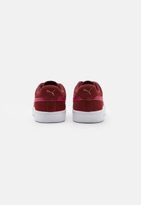 Rood suède sneakers met een witte rubberen zool, voorzien van een gouden logoaccent en een gewatteerde kraag voor extra comfort. De achterkant toont een gladde afwerking.
