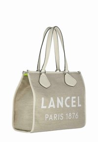 Sac fourre-tout tissé beige avec l'inscription blanche "LANCEL PARIS 1876", accents en cuir blanc contrastants, double anses et une forme structurée.