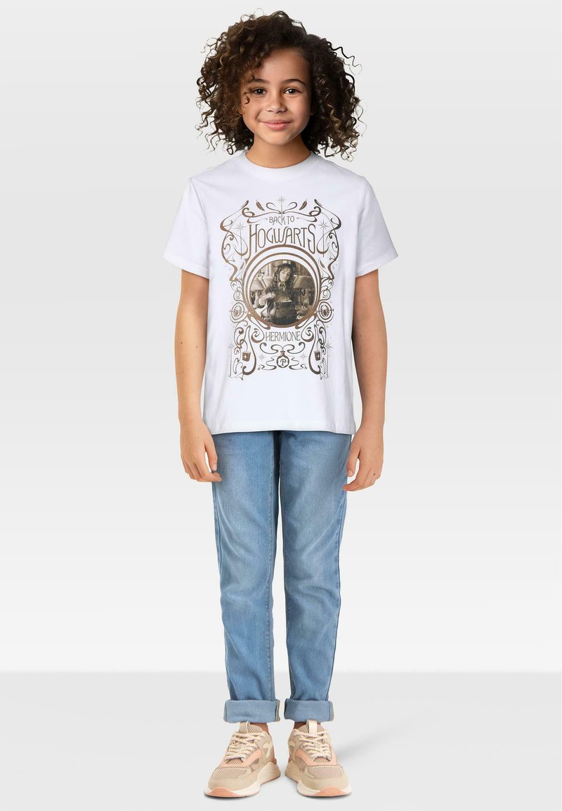 Biała koszulka z graficznym nadrukiem przedstawiającym "Powrót do Hogwartu" oraz wizerunek Hermiony, w połączeniu z jasnoniebieskimi dżinsami i beżowymi trampkami.
