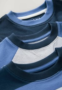 Kolme crewneck t-paitaa pinoitettuna, tummansinisena, vaaleansinisena ja harmaana. Puuvillakangasta, jossa on ribattu kaula-aukko ja sileä rakenne.