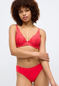 Rdeč čipkast modrček s cvetličnim vzorcem, ki ima na sredini poudarjen lok. Ujemajoče se rdeče hlačke z čipkastim robom na pasu.