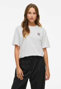T-shirt bianca a maniche corte con ricamo "SUN DAY" in marrone scuro, abbinata a pantaloni neri a vita alta. Design semplice, vestibilità rilassata.