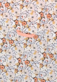 Bloemmotief stof met een lichtroze achtergrond bevat kleine, gekleurde bloemen in wit, oranje en bruin. Inclusief een klein oranje label.