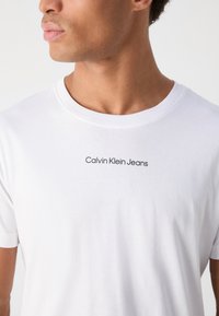 White cotton t-shirt featuring a crew neckline and short sleeves, with "Calvin Klein Jeans" logo printed in black on the chest.