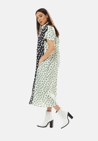 Dress featuring a half black and half white design with green spots, knee-length, short sleeves, and side pockets. Paired with white heeled boots.