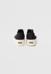 Scarpe platform in tela nera con una superficie testurizzata, dotate di una suola in gomma bianca, marchio sul tallone e un design a scollo basso.
