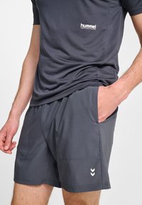 Szary zestaw koszulki i spodenek sportowych z prążkowaną teksturą, kieszeniami po bokach oraz białym logo marki na koszulce i spodenkach.