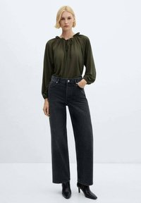 Jeans largi de culoare gri închis, asociați cu o bluză lejeră de culoare verde măsliniu, cu un guler strâns cu un șnur. Botine negre cu toc finalizează ținuta.