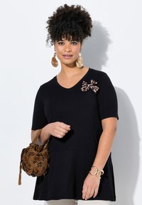 Mustat lyhythihaiset puserot V-päällä ja leopardikuosisella nauhalla olkapäällä, yhdistettynä tekstuuriseen ruskeaan helmikassiin.