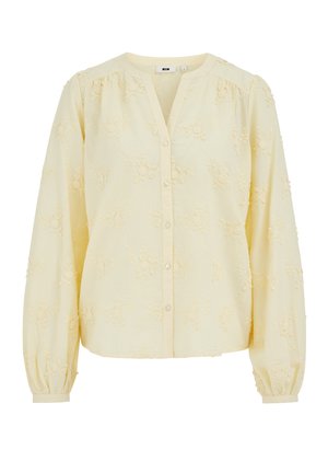 Vaaleankeltainen, pitkähihainen paita, jossa on kukkakirjailu, pyöreä pääntie, joka on V-muotoinen leikkaus, napillinen etuosa ja kerätyt hihansuut.