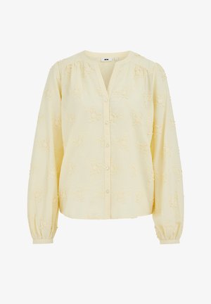 Vaaleankeltainen, pitkähihainen paita, jossa on kukkakirjailu, pyöreä pääntie, joka on V-muotoinen leikkaus, napillinen etuosa ja kerätyt hihansuut.