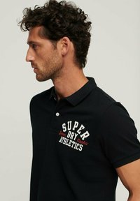 Polo nero a maniche corte, con logo rosso e bianco ricamato sul petto, tessuto testurizzato e colletto abbottonato.