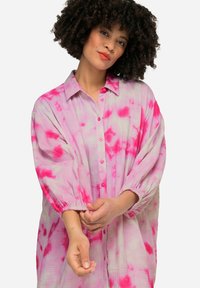 Blusa leggera e fluida, di taglio ampio, in un motivo tie-dye rosa e bianco; presenta un colletto, chiusura con bottoni e polsini elasticizzati.