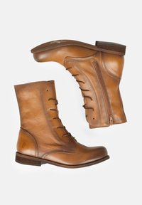 Botas de tobillo de cuero marrón con punta redonda, cordones en la parte delantera y cremallera lateral. Presentan un acabado texturizado y un tacón bajo apilado.