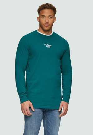 Tiefblaues Langarm-T-Shirt aus Baumwolle mit einem weißen Logo-Druck auf der Brust und enganliegenden Bündchen, kombiniert mit hellblauen Jeans.
