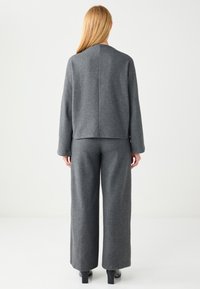 Maglione grigio di lana con vestibilità rilassata e maniche lunghe, abbinato a pantaloni grigi a gamba larga, entrambi caratterizzati da una texture morbida.