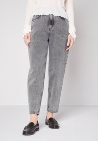 Graue High-Waist-Jeans mit einem lockeren Schnitt, die ein verblasstes Finish und sichtbare Nähte aufweisen. Kombiniert mit schwarzen Loafers.