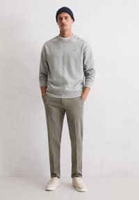 Grijze sweatshirt met ronde hals, gecombineerd met lichtgrijs-groene broek. Het model draagt een donkere gebreide beanie en lichte sneakers. Gelaagde stof.