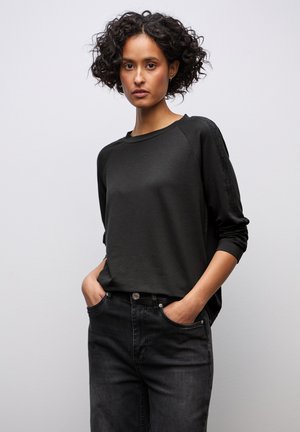 Maglietta nera a maniche lunghe con maniche raglan, realizzata in tessuto liscio, abbinata a jeans in denim scuro con bottone anteriore e tasche.