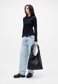 Námornícky rebrovaný kardigan, svetlomodré vysoké džínsy, čierna kožená taška, masívne čierne topánky. Jednoduchý dizajn s gombíkovým zapínaním a golierom.