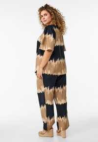 Twee-delige outfit bestaande uit een top met korte mouwen en wijdvallende broek. Gemaakt van zachte stof in zwart en beige met een scherp patroon.