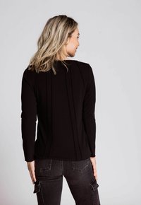 Schwarzes, geripptes Langarmoberteil mit Rundhalsauschnitt, das vertikale Nähte und eine subtile Textur aufweist, kombiniert mit dunkelgrauen Cargo-Hosen.