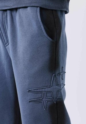 Close-up van blauwe broek met een voorkwauw en gestikte abstracte sterontwerpen op de dij.