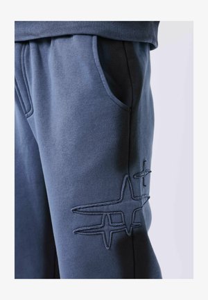 Close-up van blauwe broek met een voorkwauw en gestikte abstracte sterontwerpen op de dij.