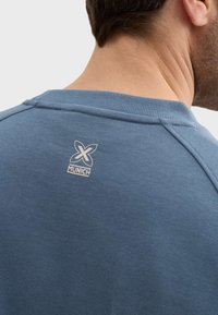 Sudadera azul con cuello redondo acanalado. Presenta un pequeño logo blanco en la parte posterior con el texto "MUNICH". Material de algodón suave, ajuste relajado.