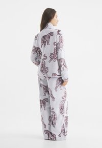 Zestaw dresowy z polarowego materiału w jasnoszarym kolorze, z wzorem w tygrysa w ciemnym bordowym kolorze. Obejmuje wysoką stójkę i luźne spodnie.