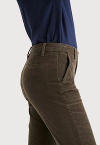 Bruna kordflortbyxor med en strukturerad vertikal ribbdesign, med framfickor och en slät midja, tillsammans med en mörkblå topp.