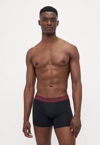 Boxers pretos com uma cinta em bordo, apresentando uma marca em relevo. O tecido parece suave e elástico, concebido para conforto e ajuste.