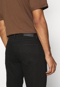 Černé džíny z denimu s úzkým střihem, s dvěma zadními kapsami a koženou nášivkou s nápisem "CLOSED" na pase.