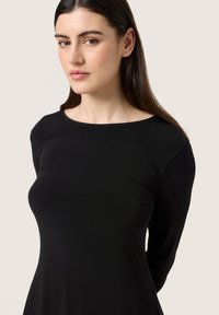 Czarna sukienka z długim rękawem i okrągłym dekoltem, wykonana z miękkiego materiału. Dopasowana góra łagodnie rozszerza się w talii. Gładka tekstura i minimalne detale wzornicze.