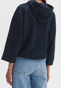 Felpa strutturata blu navy con cappuccio ampio, spalle scese e vestibilità ampia, abbinata a jeans a vita alta azzurri chiari con tasche posteriori.